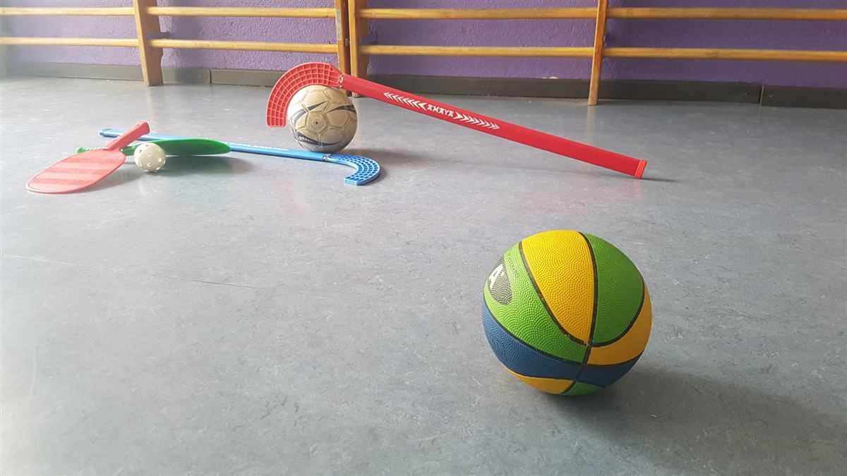 Stick, pala, pelotas y balón de baloncesto en el suelo del gimnasio del colegio