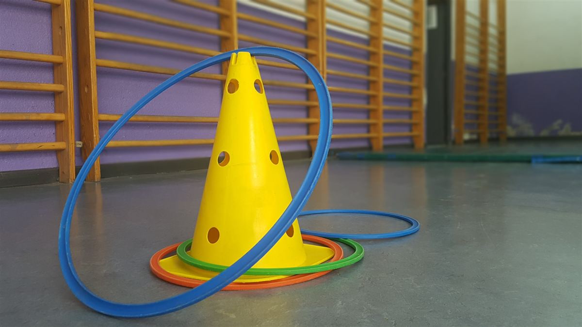 Cono y aros de colores en el suelo del gimnasio del colegio, junto a las espalderas