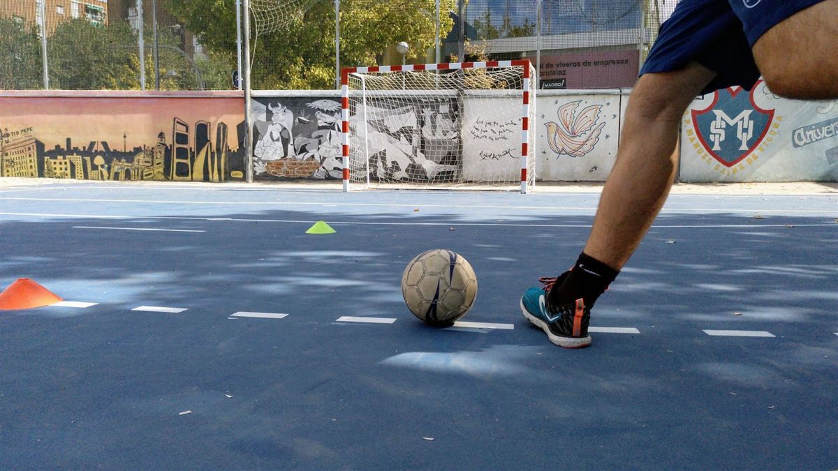 Balón de fútbol sala en la pista del colegio, con los murales y el escudo del colegio al fondo